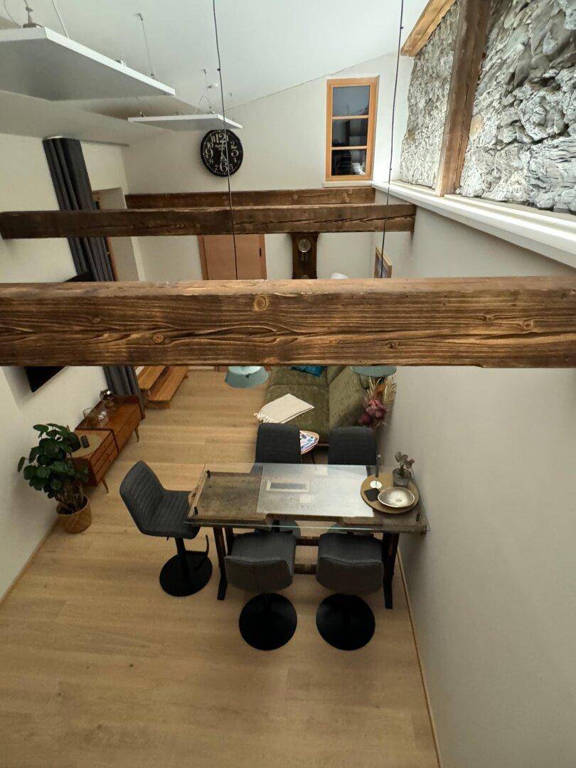 Weitwinkelansicht von oben auf den offenen Wohn-Essbereich mit Holzbalken und einem modernen Esstisch.