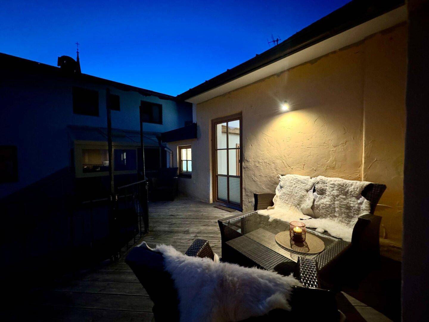 Weitläufiger Terrassenbereich am Abend mit bequemen Sitzgelegenheiten und indirekter Beleuchtung an der Hausfassade.
