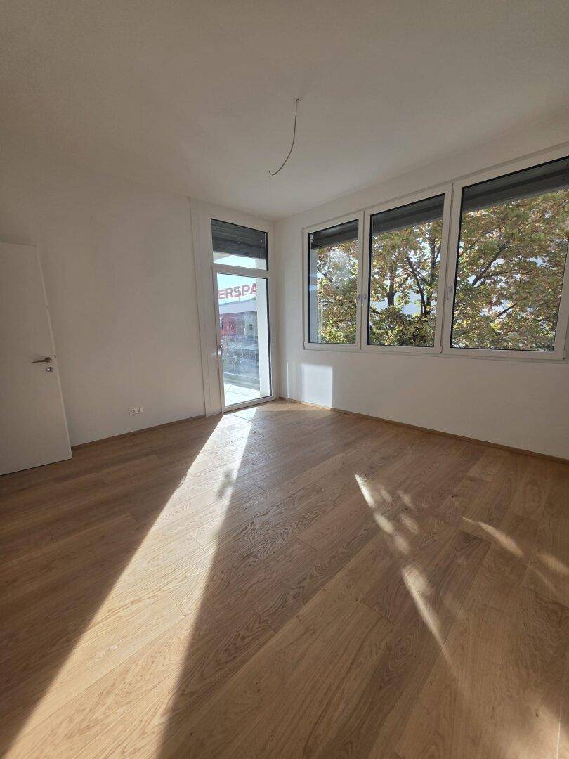 Heller Wohnraum mit neuem Parkettboden und großen Fenstern, die viel Tageslicht hereinlassen.