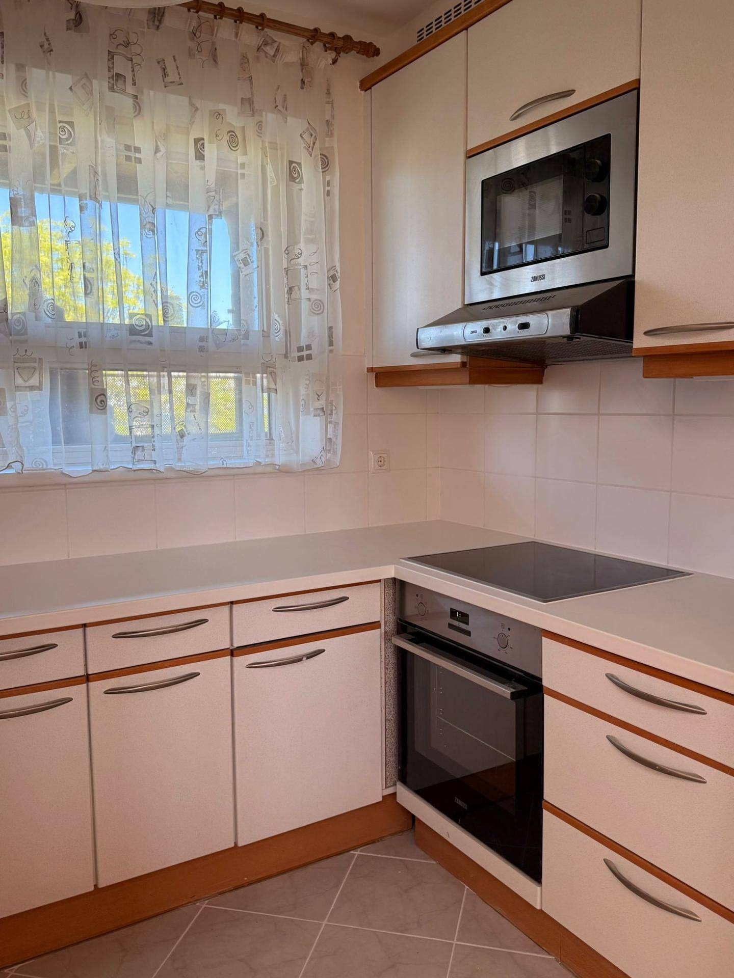 Funktionale Küche mit weißen Schränken, Einbaugeräten und einem Fenster.