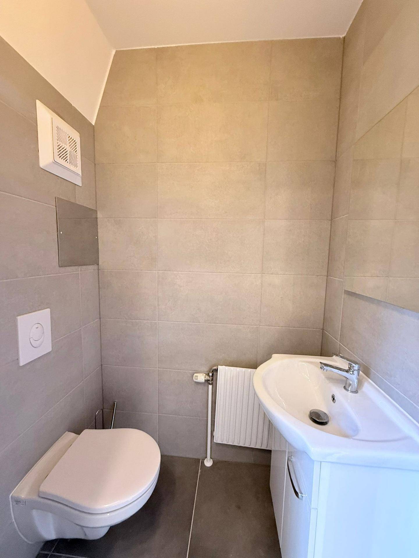 Kleines Gäste-WC mit Wand-WC, Waschbecken und grauen Fliesen.