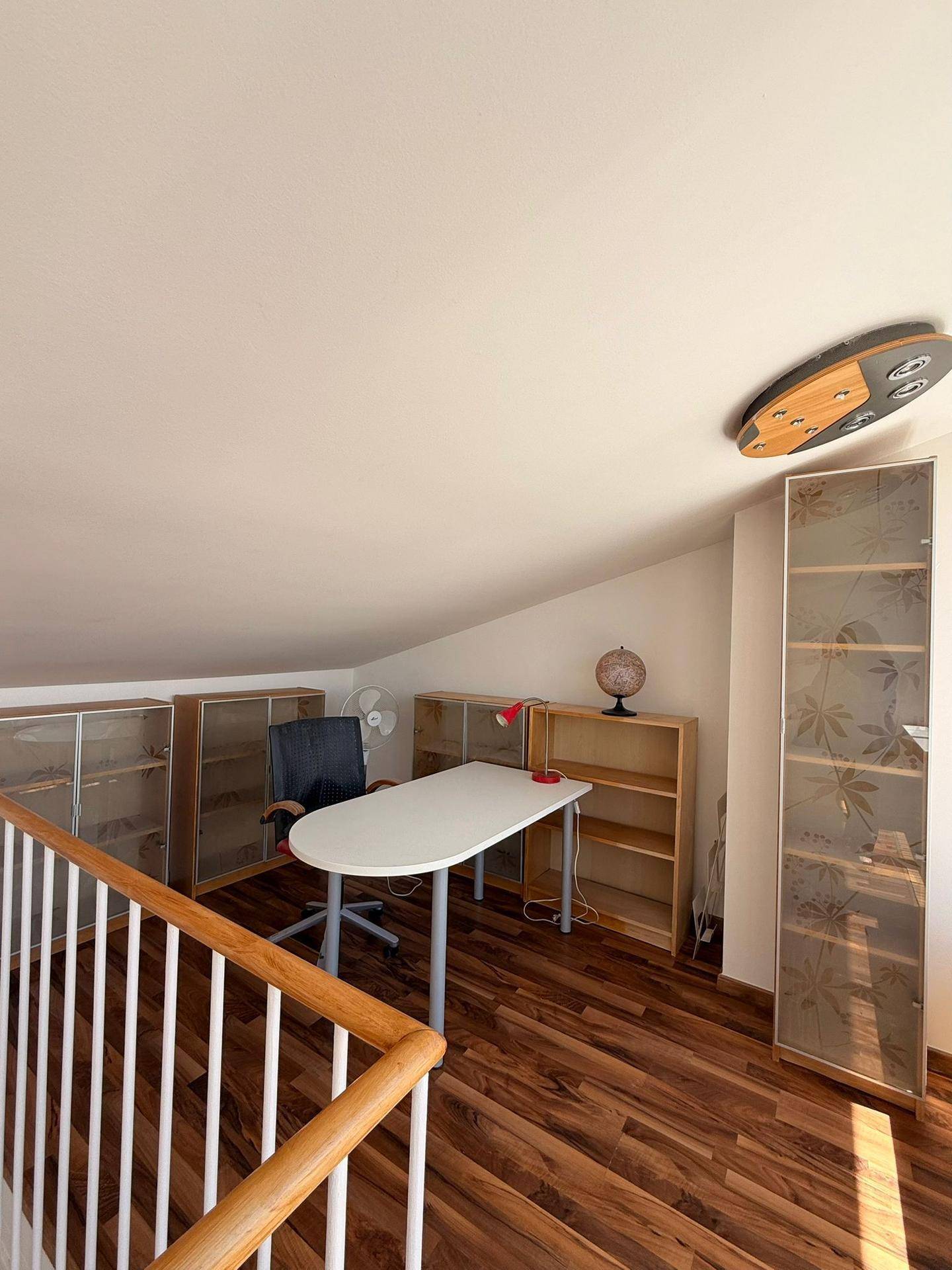 Helles Arbeitszimmer im Dachgeschoss mit Schreibtisch, Regalen und schrägen Wänden.