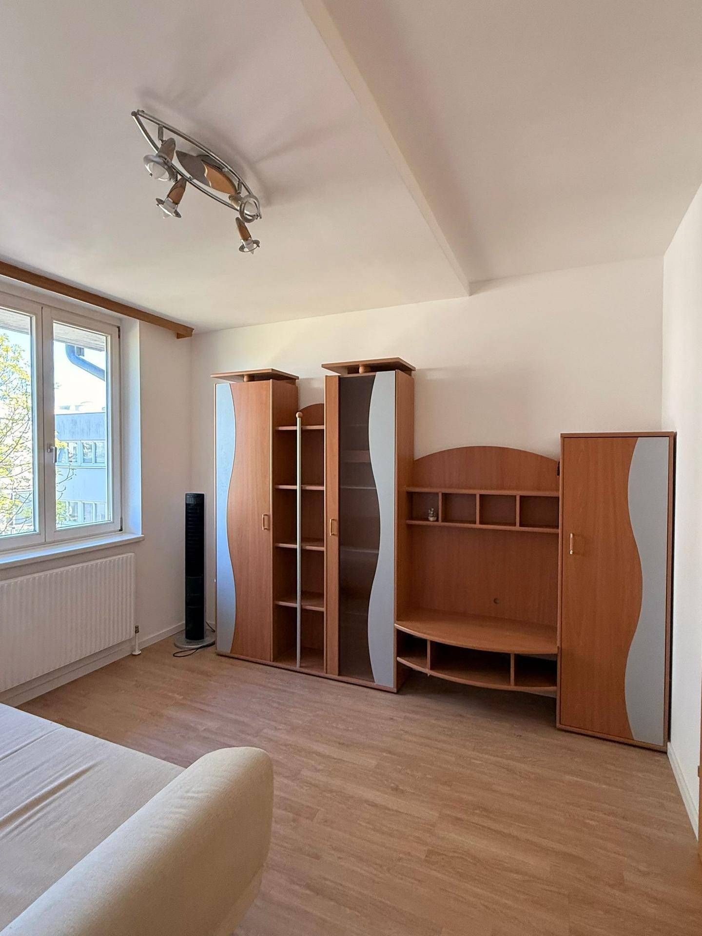 Schlafzimmer mit Holzmöbeln, Laminatboden und einem großen Fenster.