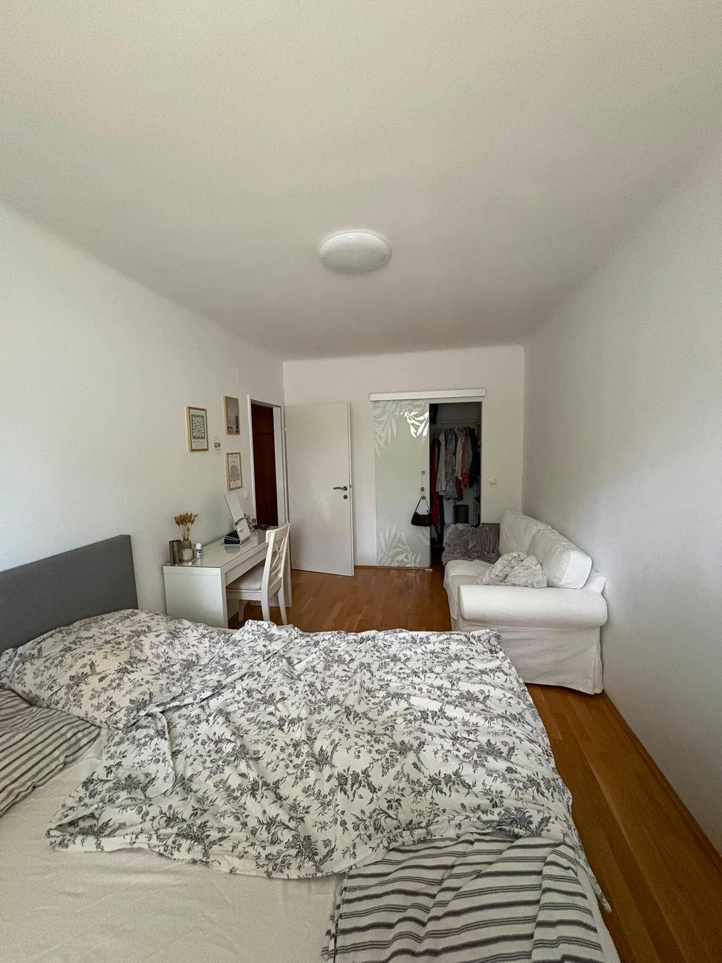 Schlafzimmer mit Bett, Schreibtisch und offenem Zugang zu einem begehbaren Kleiderschrank.
