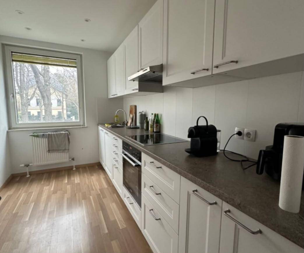 Funktionale Küche mit weißen Schränken, Fenster und Heizkörper, bietet eine angenehme Kochumgebung.