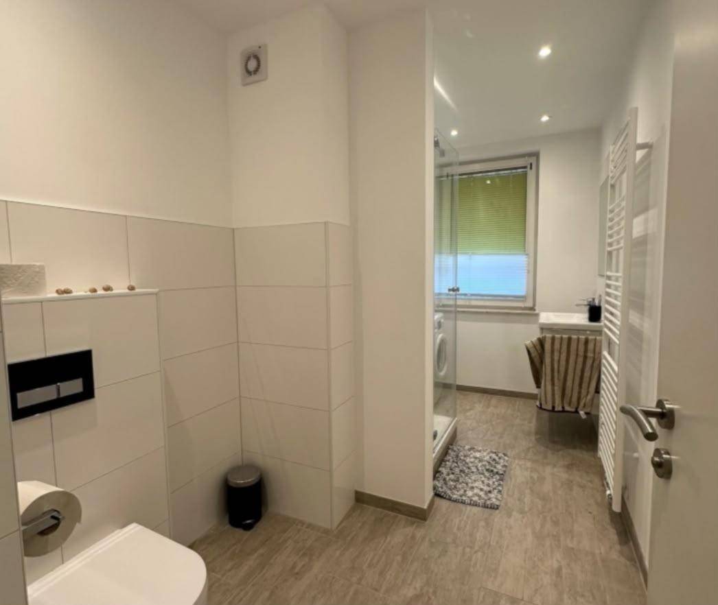 Helles Badezimmer mit Dusche, WC, Waschbecken und beheiztem Handtuchhalter, ausgestattet mit Fenster.