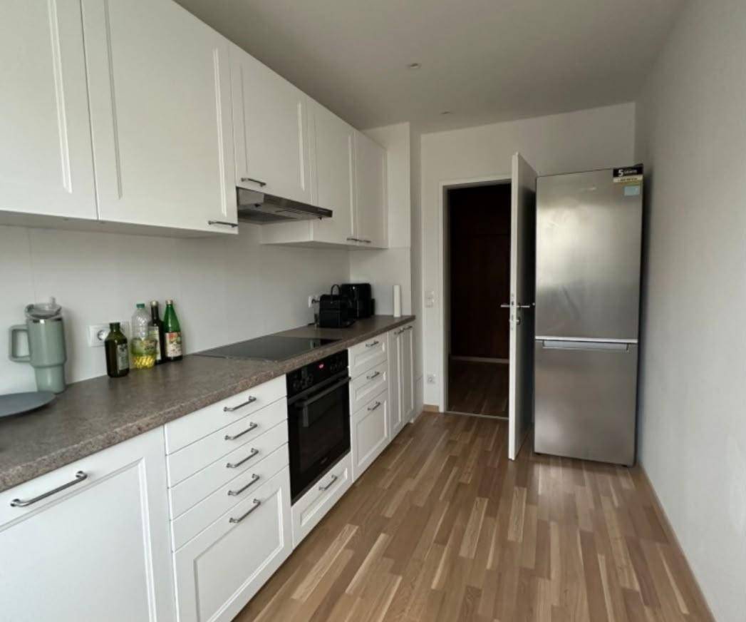 Moderne Küche mit weißen Schränken, dunkler Arbeitsplatte und integrierten Geräten, inklusive Kühlschrank.