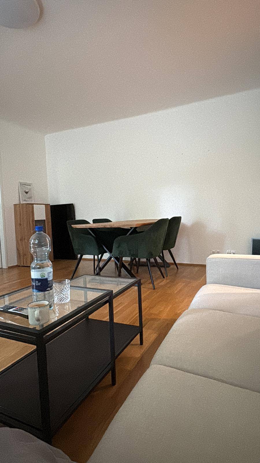 Essbereich mit Holztisch und modernen grünen Stühlen, angrenzend an das Wohnzimmer.