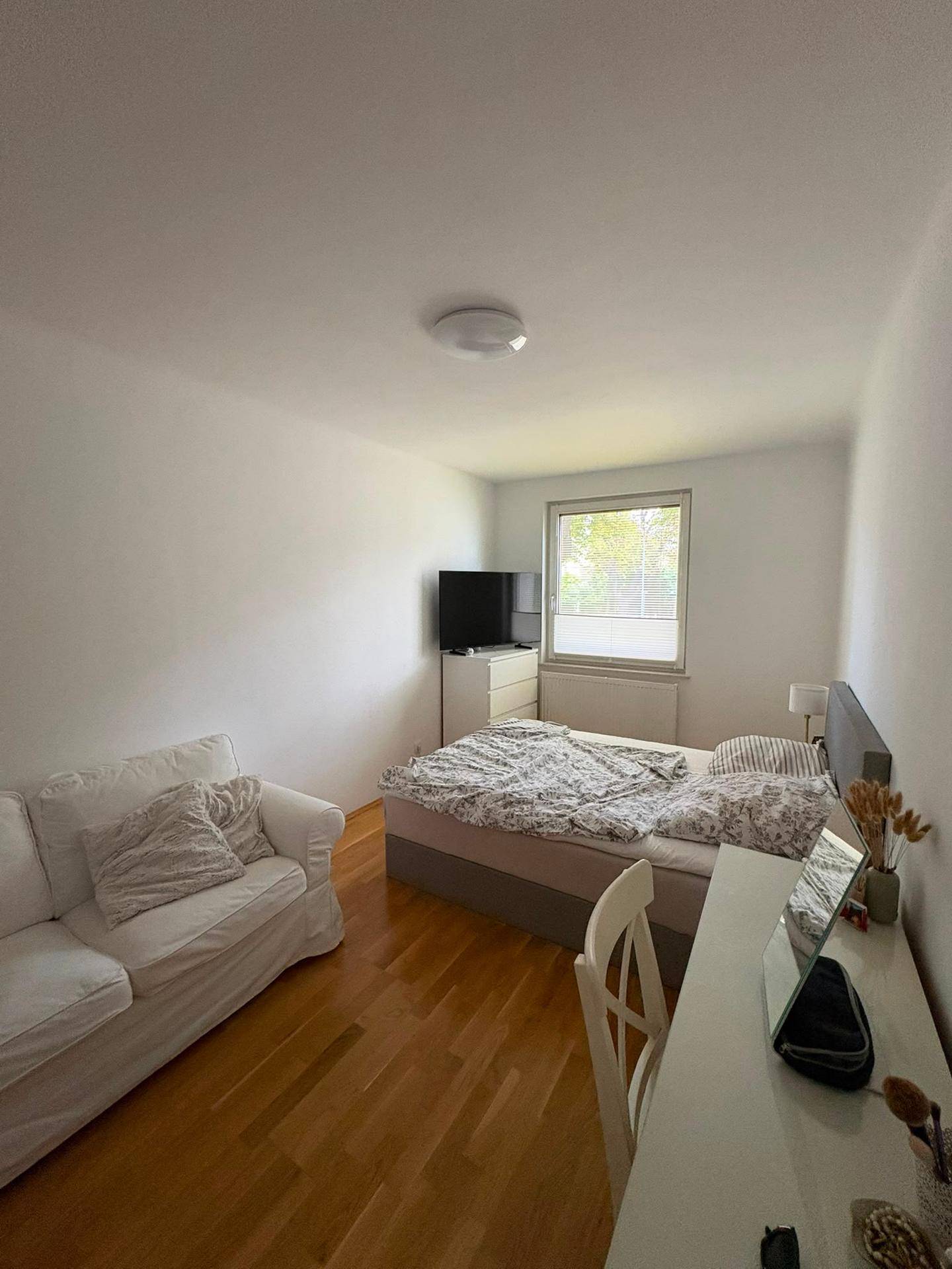 Schlafzimmer mit Doppelbett, kleinem Sofa, Schreibtisch und Fenster mit Blick ins Grüne.