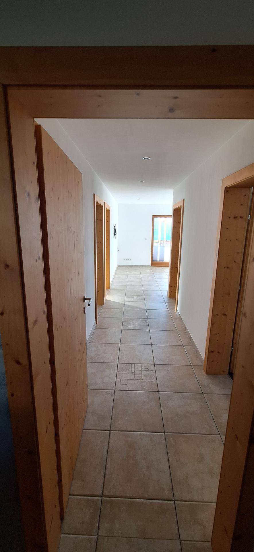 Langer Flur mit Fliesenboden und Holztüren, der zu verschiedenen Räumen führt.
