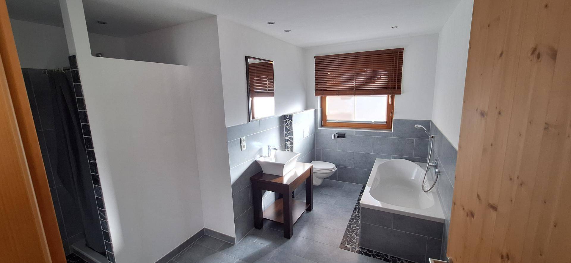 Modernes Badezimmer mit Badewanne, Waschtisch, WC und Fenster mit Holzjalousie.