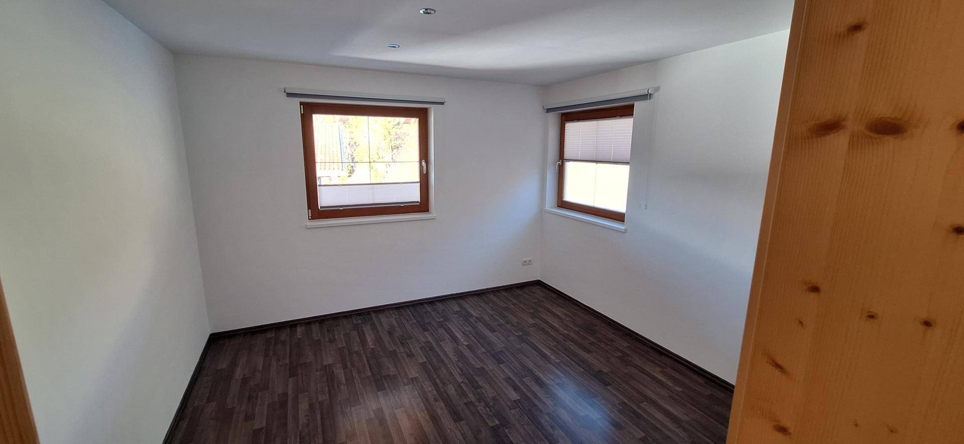 Gemütliches Schlafzimmer mit dunklem Laminatboden und zwei Fenstern für natürliches Licht.