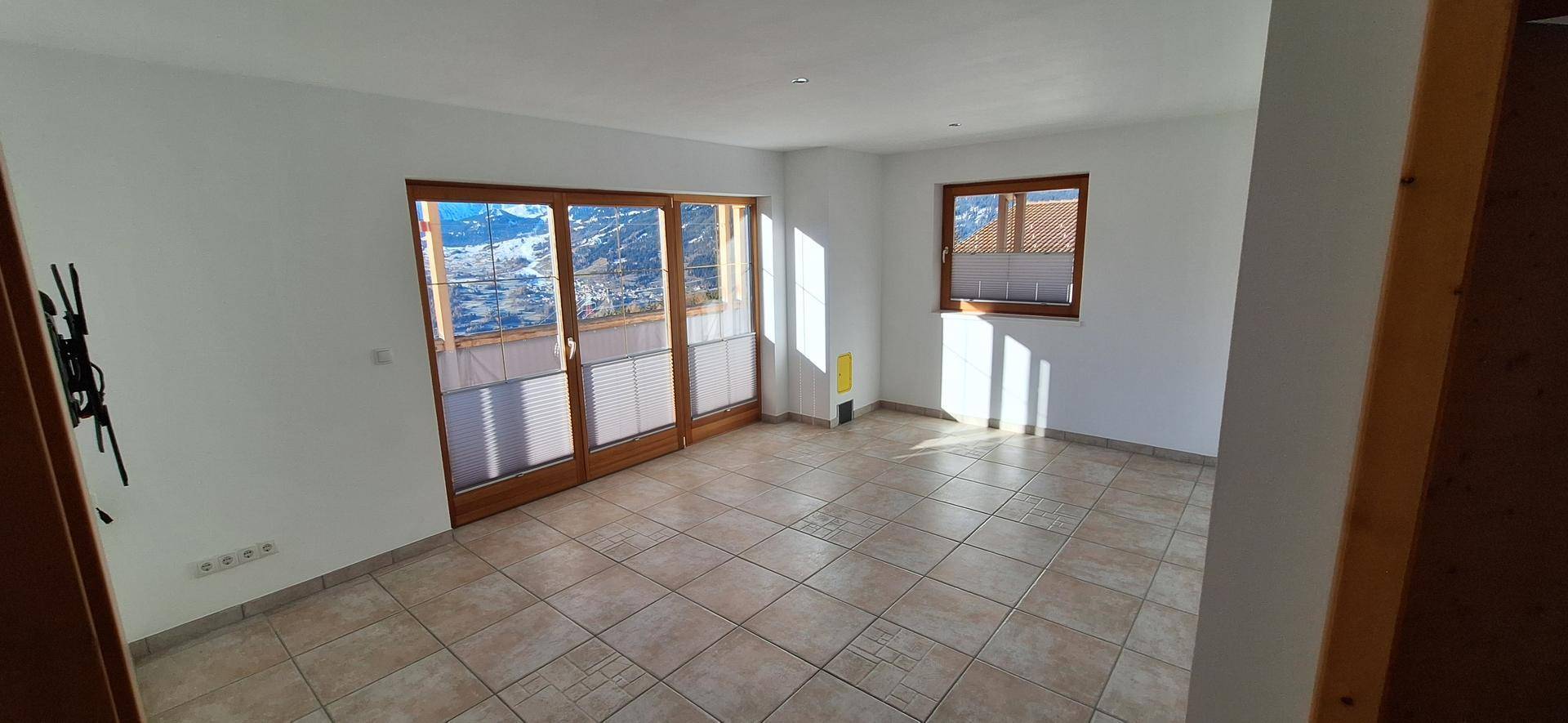 Heller Wohnraum mit Fliesenboden und großem Schiebefenster mit Bergblick.