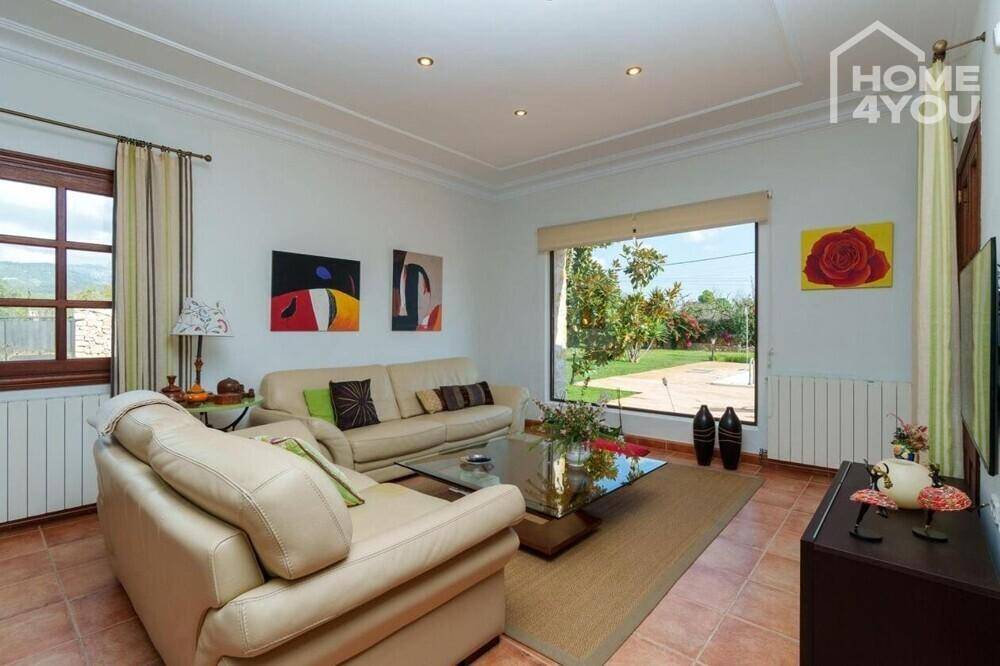 Geräumiges Wohnzimmer mit beigen Sofas, Terrakottaboden und Blick auf den Garten und Pool.