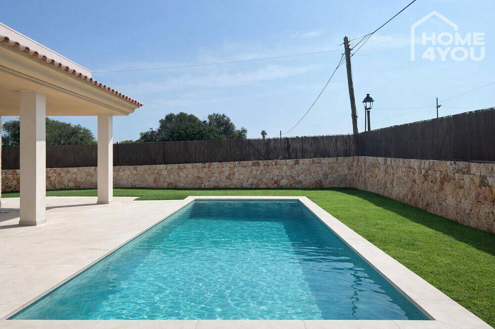 Langer, rechteckiger Pool umgeben von Rasen und einer Steinmauer.
