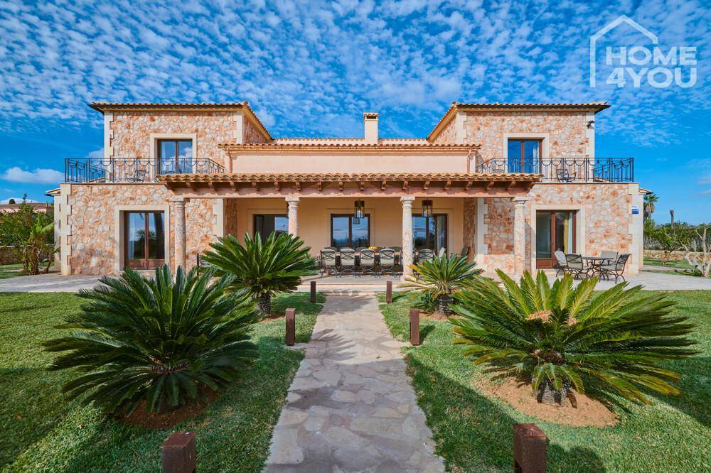 Elegante Steinfassade der Villa mit Säulen und gepflegtem Gartenweg unter blauem Himmel.