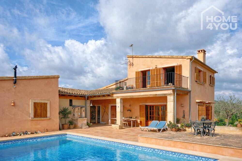 Traditionelles Landhaus mit Pool, Terrasse und Balkon unter blauem Himmel.