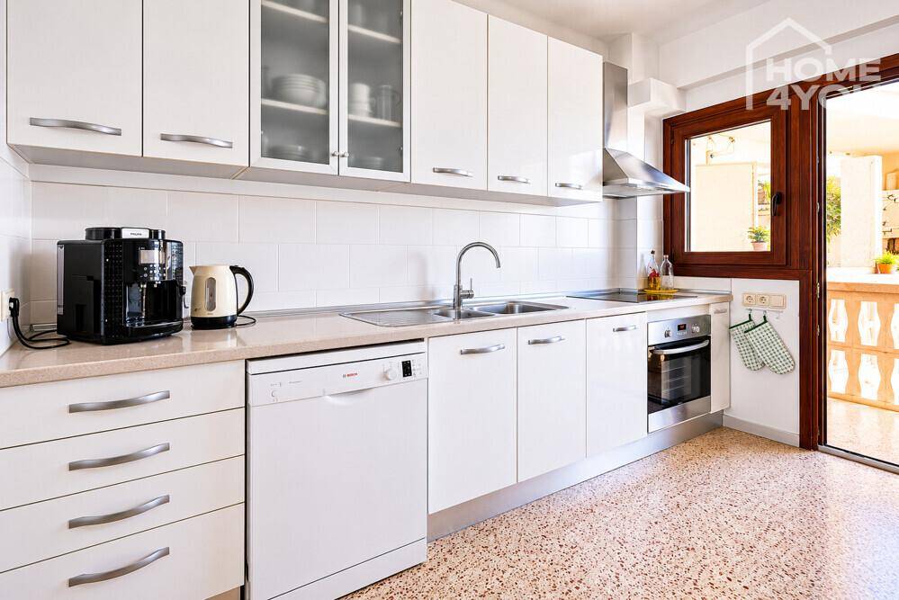 Moderne weiße Küche mit Einbaugeräten, Spülmaschine und Zugang zum Außenbereich.