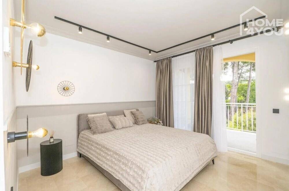 Helles Schlafzimmer mit Doppelbett, Zugang zum Balkon und modernen Leuchten.