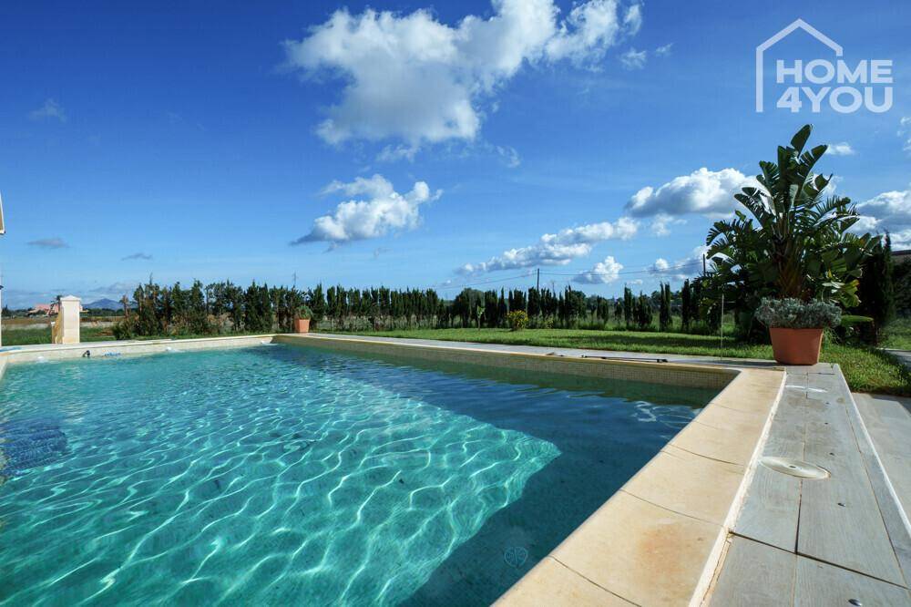 Der erfrischende Poolbereich mit blauer Wasseroberfläche und Blick ins Grüne unter strahlend blauem Himmel.