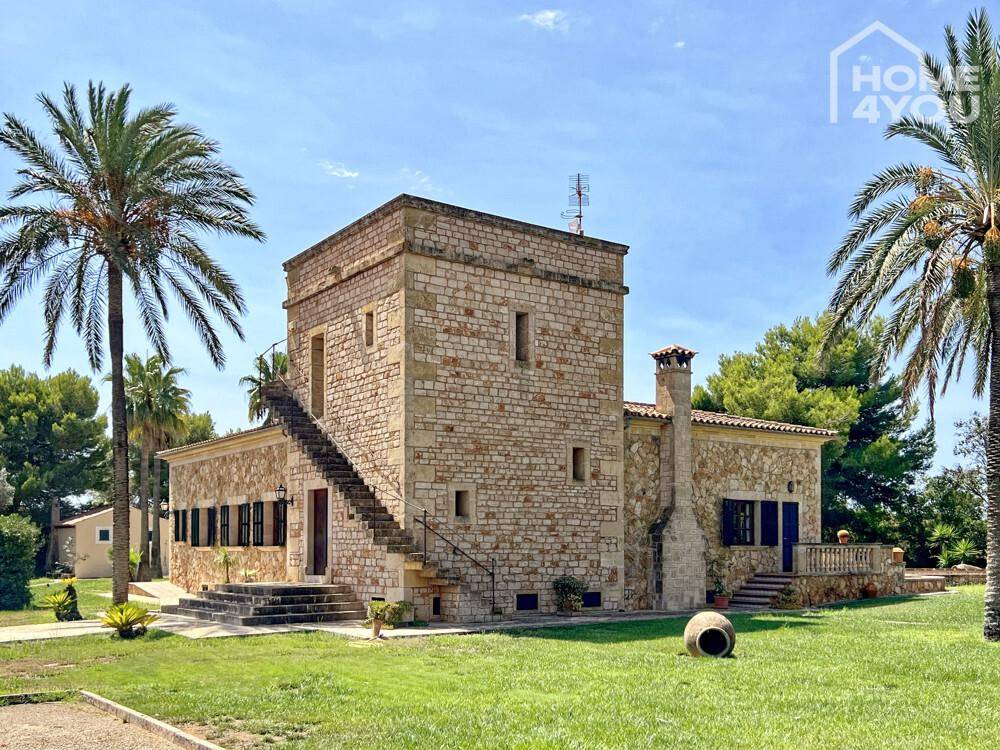 Ansicht des traditionellen Steinhauses mit markantem Turm, Außentreppe und weitläufigem Rasenbereich.