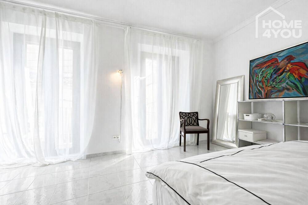 Helles Schlafzimmer mit großen Fenstertüren, die viel Tageslicht hereinlassen, und einem Spiegel.