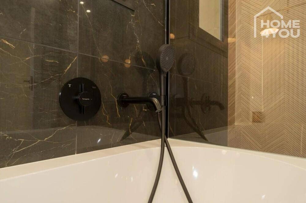 Elegantes Badezimmer mit dunklen Marmorfliesen, Badewanne und modernen Armaturen.
