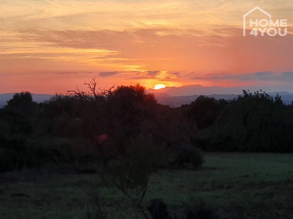 Dramatischer Sonnenuntergang über einer dunklen Landschaft mit Bergen am Horizont.