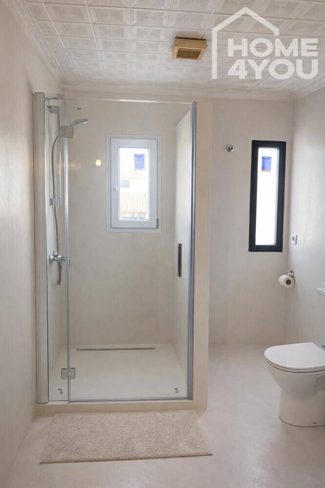 Helles Badezimmer mit Dusche, Toilette und Fenster, das Tageslicht hereinlässt.