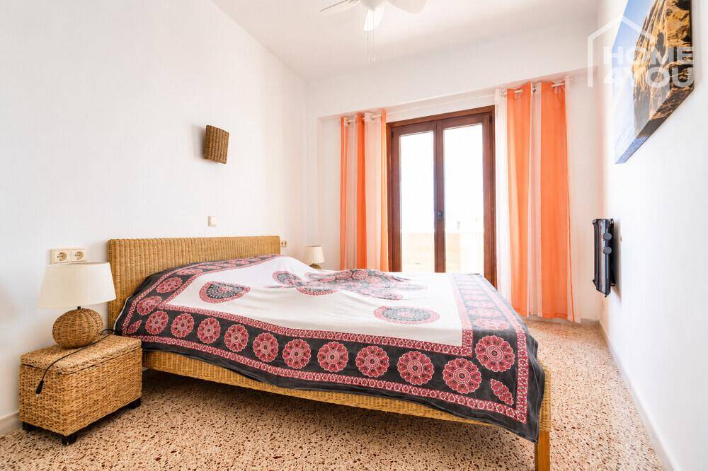 Schlafzimmer mit Rattanbett, Deckenventilator und Zugang zum Balkon.