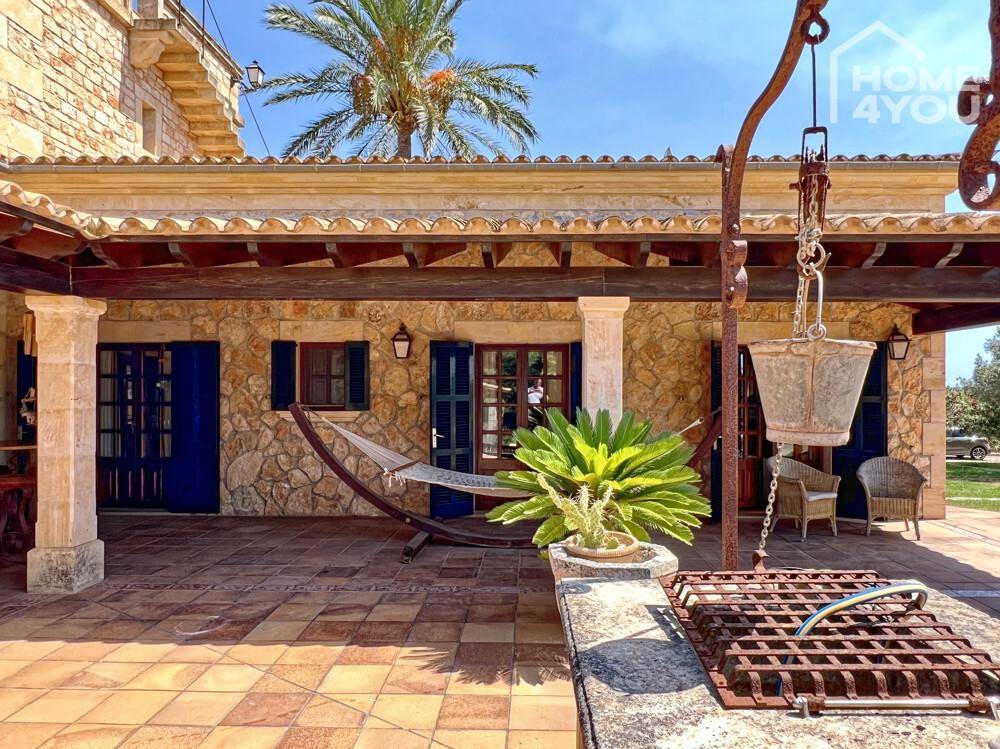 Überdachte Terrasse mit Hängematte, Topfpflanzen und einem traditionellen Brunnen, ideal zum Entspannen.