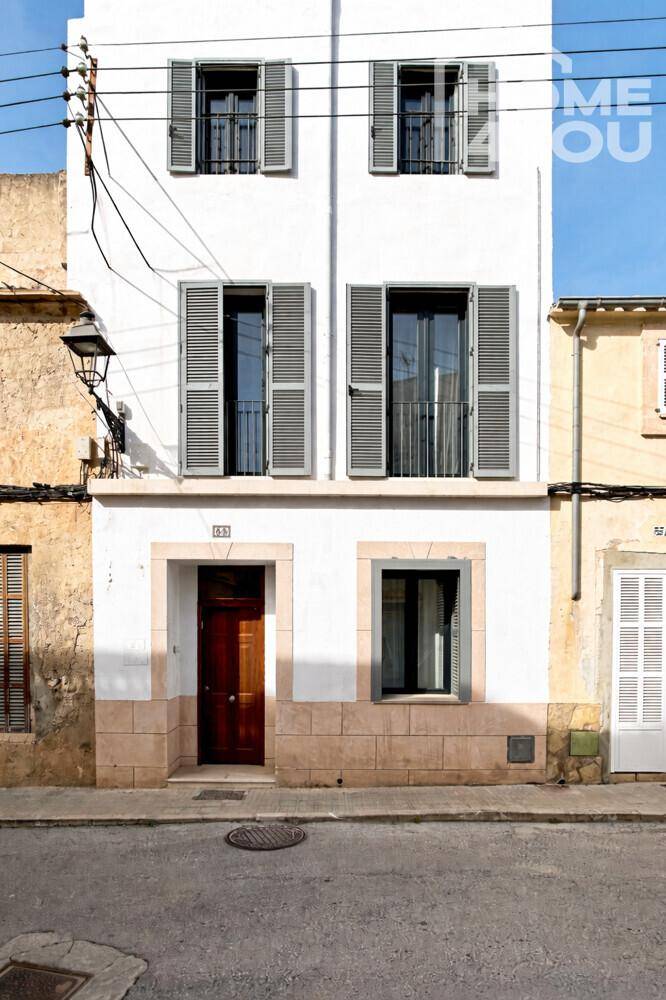 Traditionelle Hausfassade mit hellen Fensterläden und Holztür in einer städtischen Umgebung.