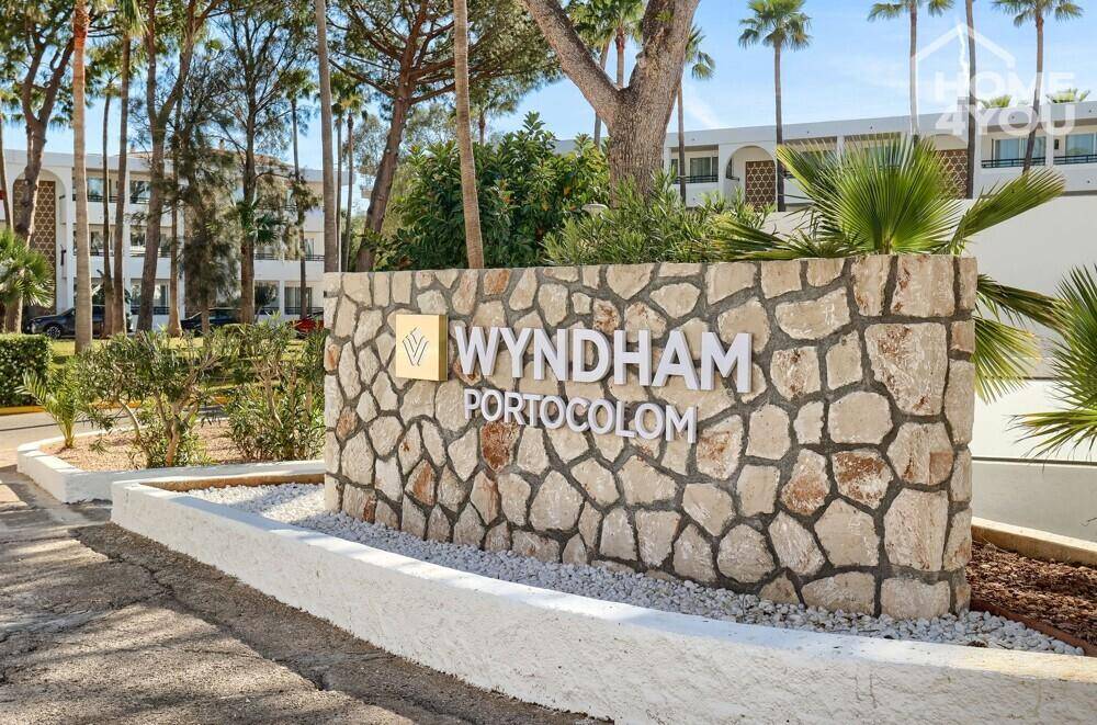Steinernes Eingangsschild des Wyndham Portocolom Resorts, umgeben von Palmen.