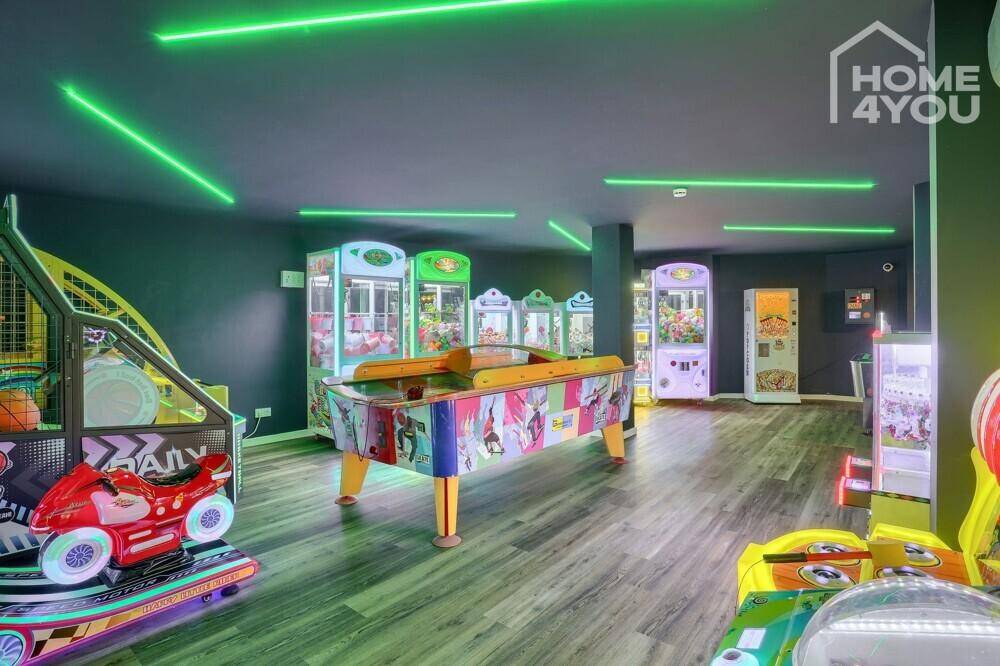 Lebhafter Spielraum mit Arcade-Automaten, Airhockey-Tisch und grüner Neonbeleuchtung.