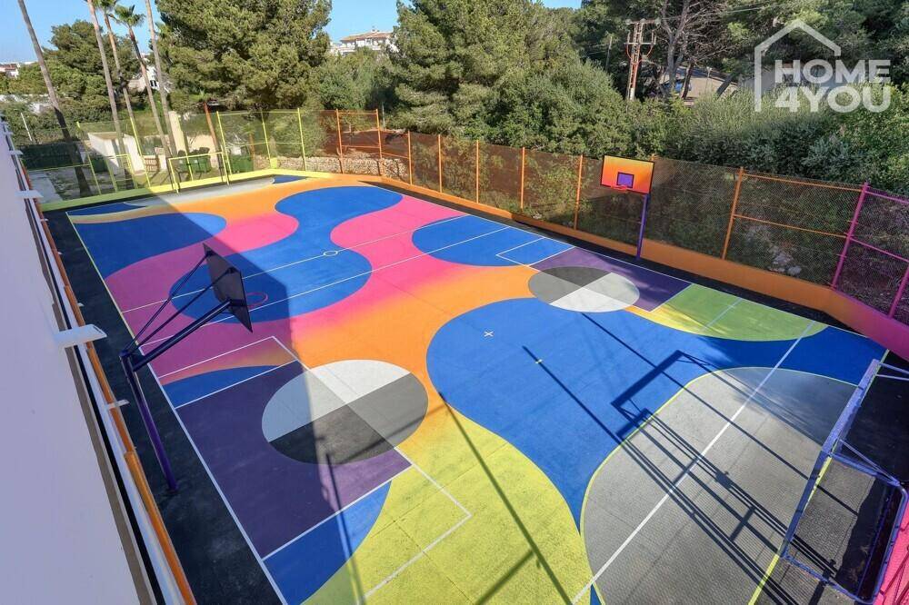 Farbenfroher Basketballplatz im Freien, umgeben von Bäumen und Zäunen.