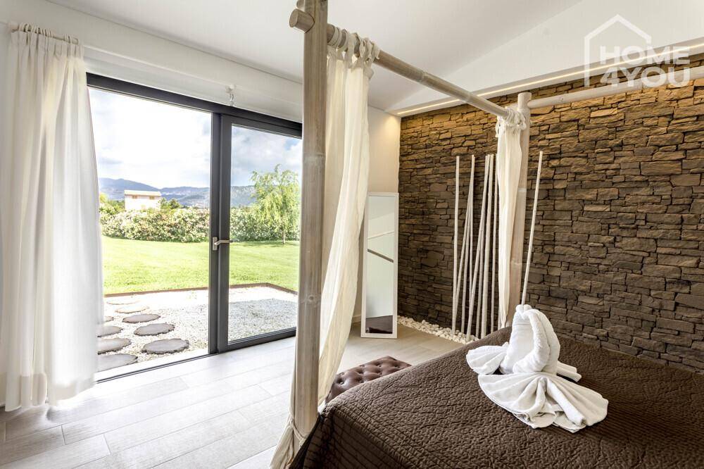 Schlafzimmer mit direktem Zugang zum Garten durch große Glastüren und Steinwand.