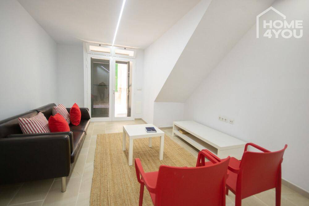 Gemütliches Wohnzimmer mit Sofa, roten Akzenten und Zugang zu einem Außenbereich.