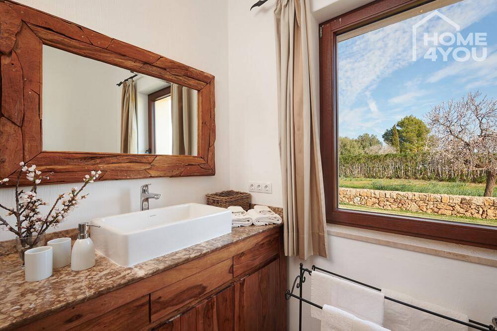 Helles Badezimmer mit Holzwaschtisch, Aufsatzwaschbecken und Fenster mit Blick ins Grüne.