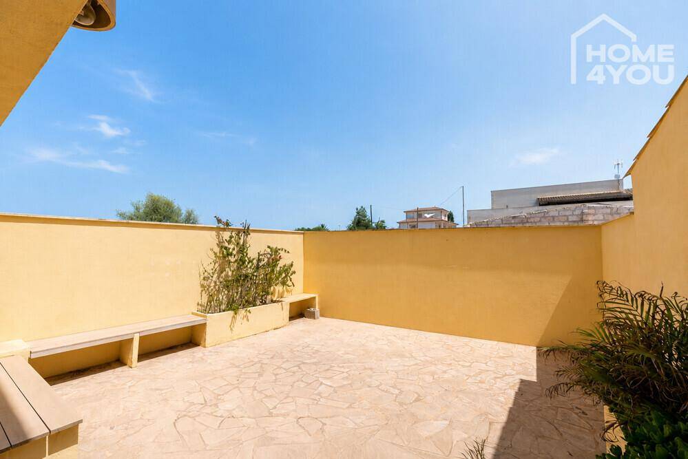 Gemütliche Terrasse mit integrierten Sitzbänken und Pflanzen, umgeben von hohen gelben Mauern.
