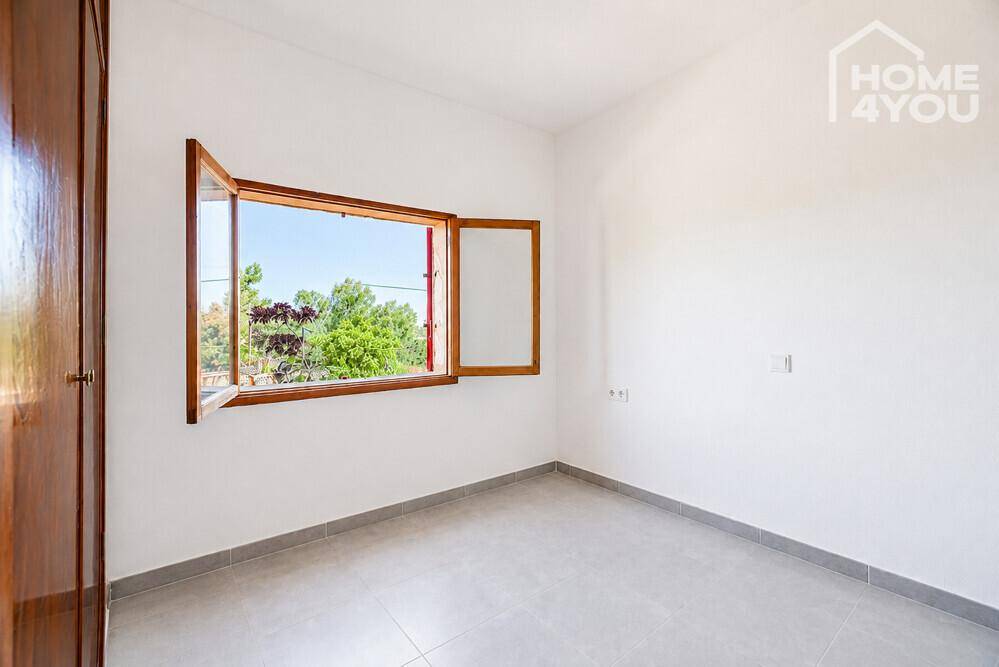 Helles Schlafzimmer mit Fliesenboden, weißen Wänden und einem Fenster mit Blick ins Grüne.