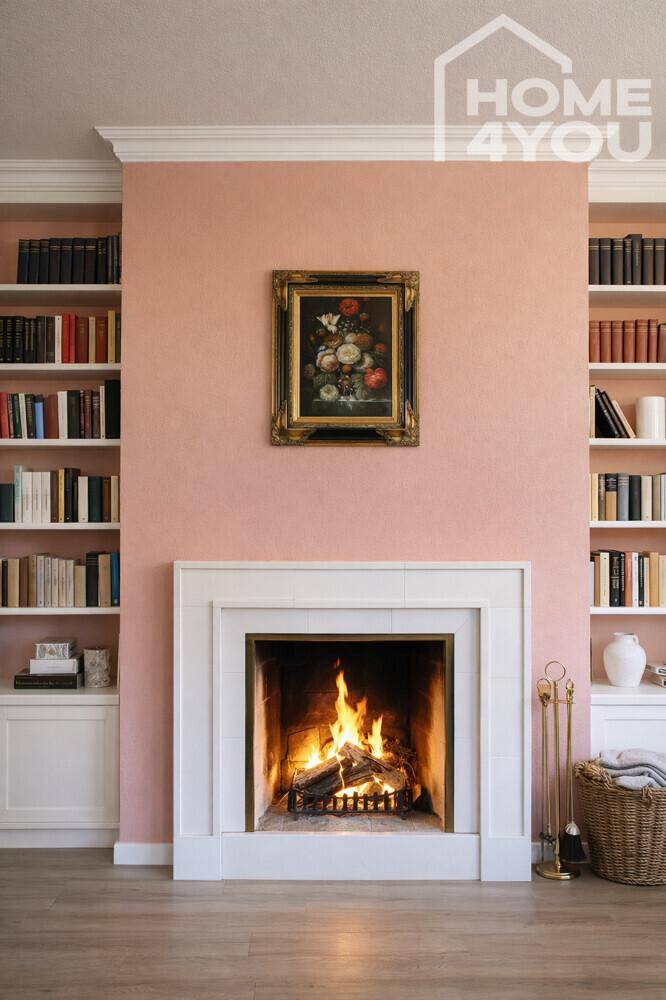 Gemütlicher Kamin mit brennendem Feuer, umgeben von Bücherregalen und rosa Wänden.