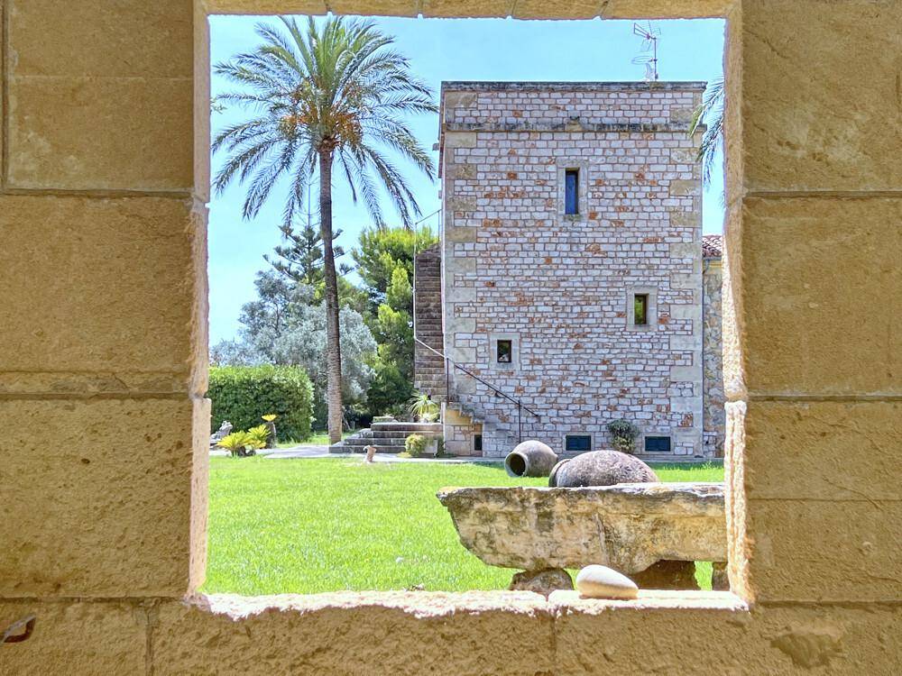 Blick durch einen Steinbogen auf den grünen Garten und das historische Gebäude im Hintergrund.