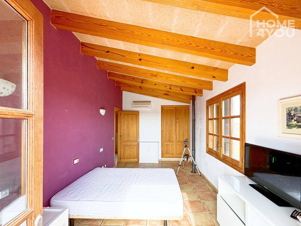 Geräumiges Schlafzimmer mit Holzbalkendecke, Fliesenboden und Blick auf die umliegende Landschaft.