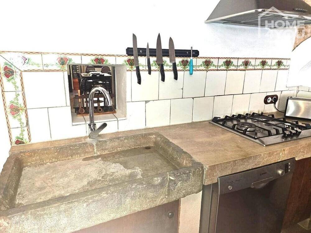 Detailansicht der Küche mit Steinspüle, Gaskochfeld und traditionellen Fliesen.