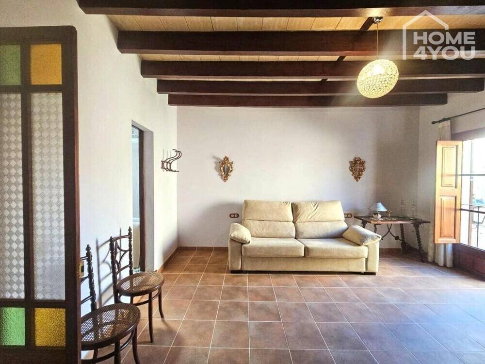 Helles Wohnzimmer mit beigem Sofa, Holzbalkendecke und Zugang zu einem kleinen Balkon.