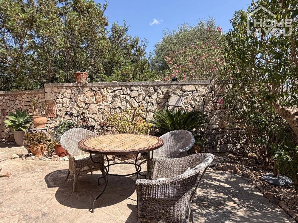 Gemütlicher Essbereich im Freien auf einer Terrasse mit Steintisch und Korbstühlen.