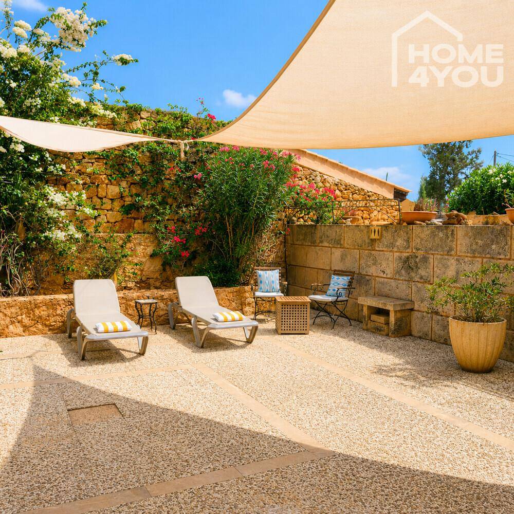 Heller Patio mit Liegestühlen und Sonnensegel, umgeben von Steinmauern und Pflanzen.
