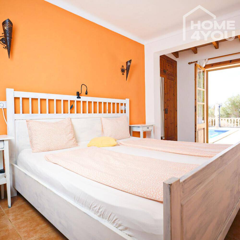 Helles Schlafzimmer mit orangefarbener Wand, weißem Bett und Blick auf den Pool.
