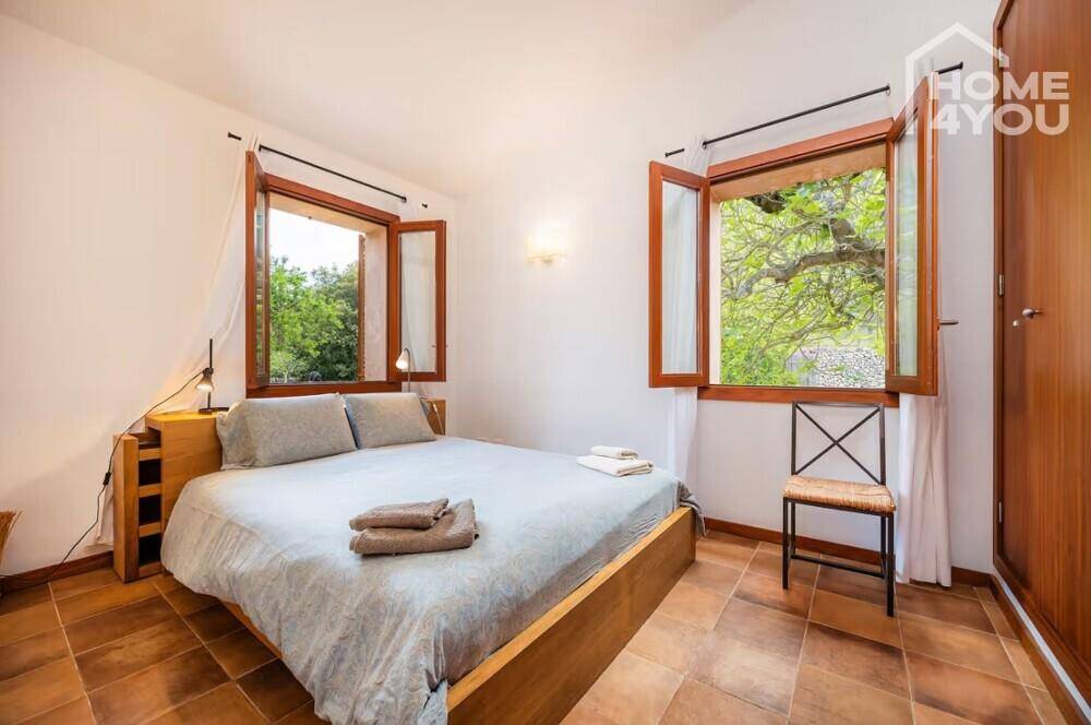 Gemütliches Schlafzimmer mit Doppelbett, Holzboden und Fenstern mit Blick ins Grüne.
