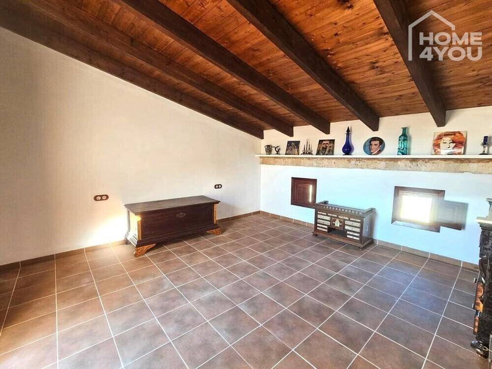 Dachgeschossraum mit sichtbaren Holzbalken, Fliesenboden und kleinen Fenstern, unmöbliert.